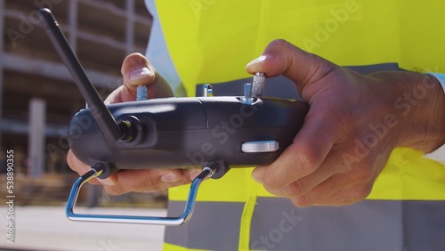 Professional drone operator in virtual reality helmet standing in front of construction site. Builder holding remote controller. Office building and crane background.