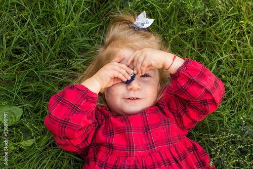 A little girl in red checkered dress lies on the green grass