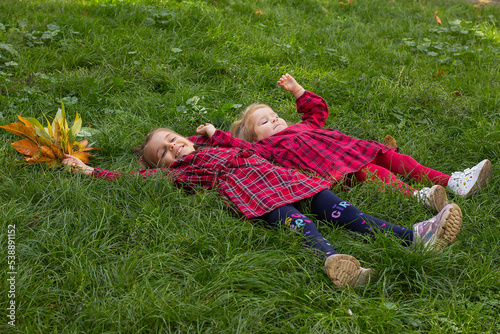 Two little girls in red checkered dresses lie on green grass