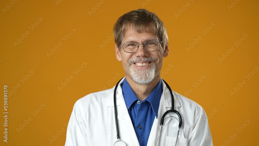 Portrait of smiling happy confident mature man medical doctor on solid yellow background.