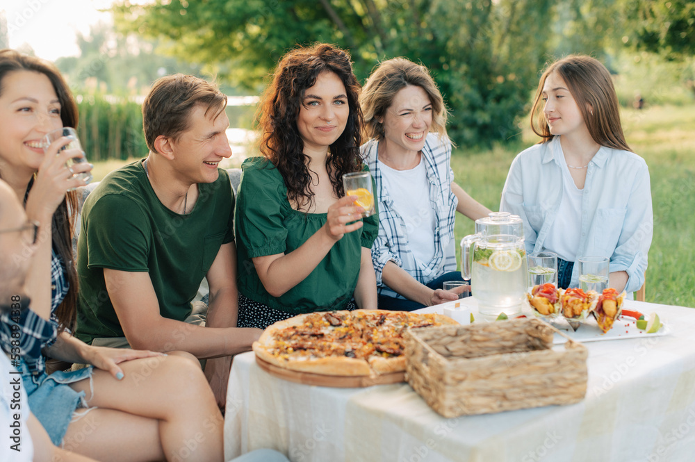 Group of friends are relaxing together outdoor. Young cheerful people clink glasses and laugh.