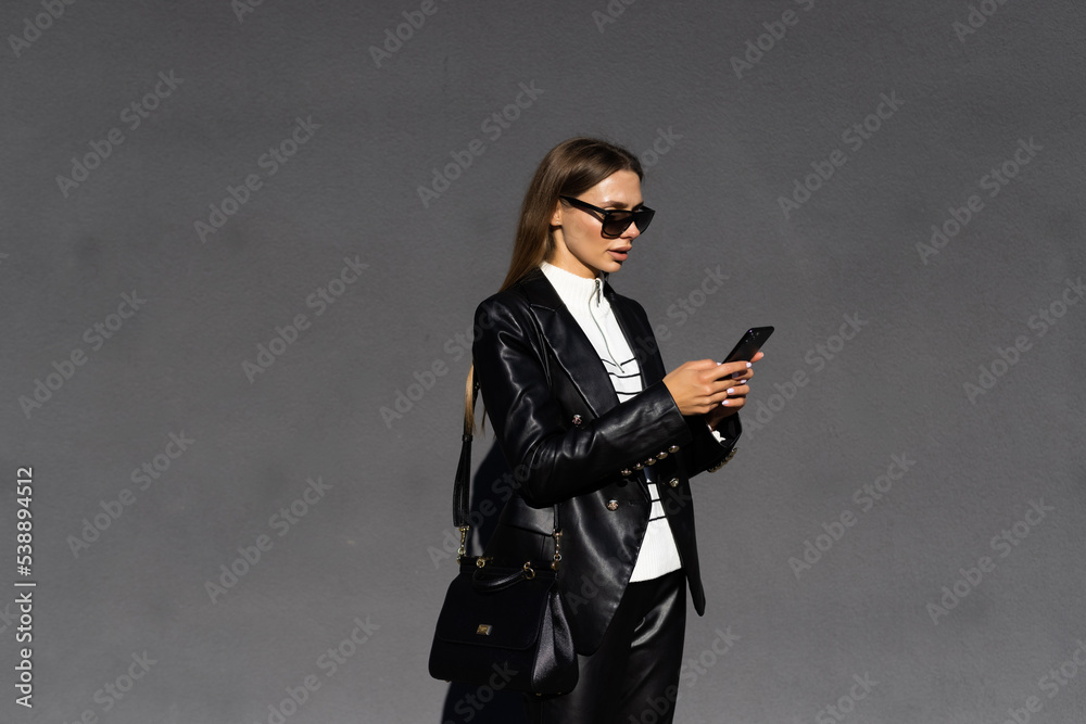 Smiling woman wearing trendy sunglasses walks down the central city street and uses her phone. Smiling woman wearing trendy sunglasses walks down the central city street and uses her phone.