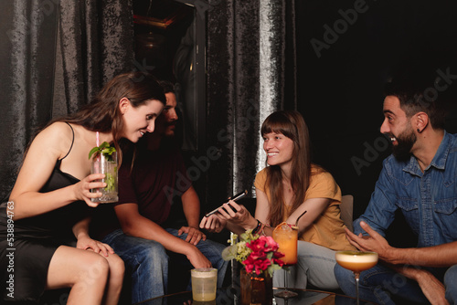 friends watching media in a smart phone in a night club while they hang out cocktails