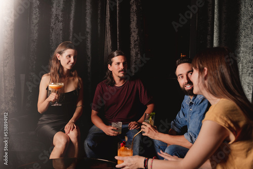 group of young friends drinking cocktails in a nightclub listening their friend
