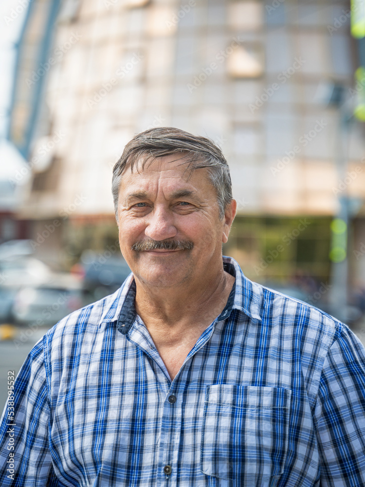 gray-haired elderly man in front of a city street. A 70-year-old man smiles gray-haired elderly man in front of a city street. A 70-year-old man smiles