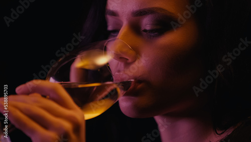 Young woman drinking white wine from glass isolated on black.