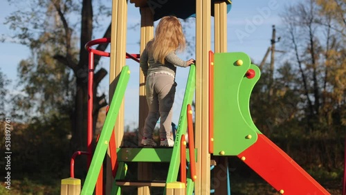 The child plays in the yard on the playground, rides on the slide, the girl is in a great mood, cheerful photo