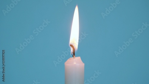Close-up of a single wax candle burning. Isolated glowing candle on a blue background. Background or illustration of a festive ceremony, a celebration, birthday or Christmas.