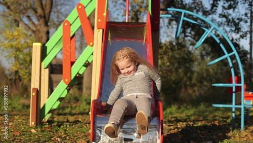 The child plays in the yard on the playground, rides on the slide, the girl is in a great mood, cheerful photo