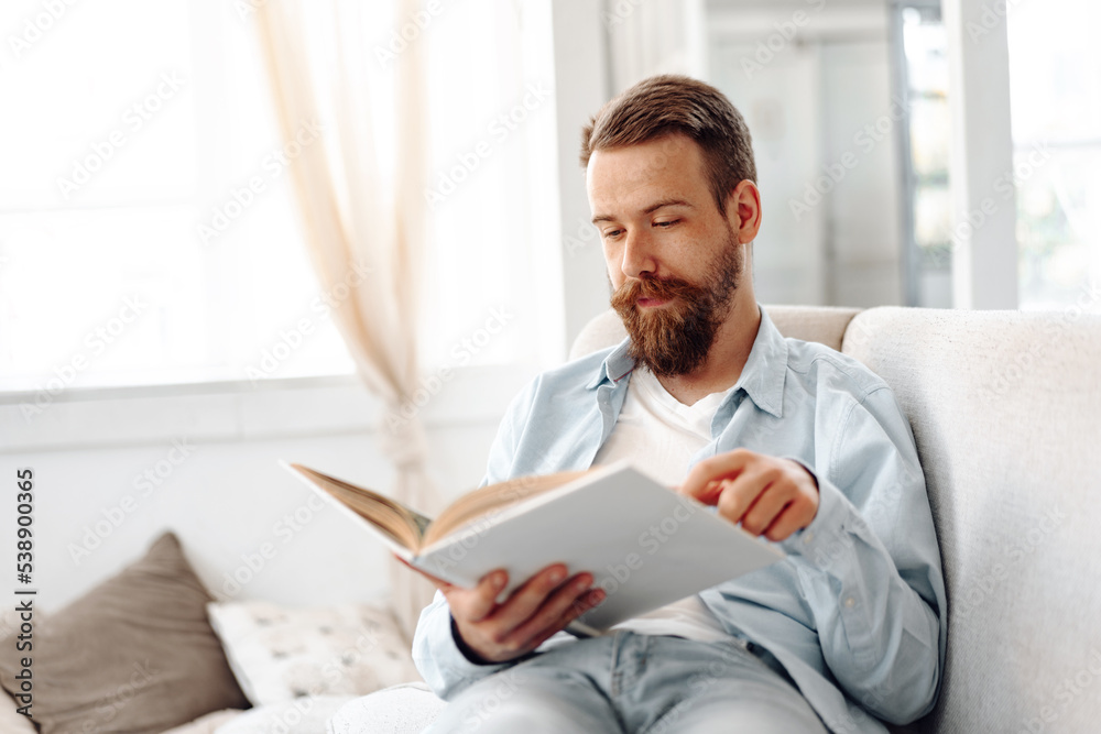 Young bearded handsome man reading book on couch at home Young bearded handsome man reading book on couch at home