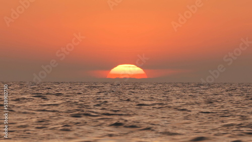 A fire red sunset with the sun behind the clouds falling into the sea by an island in the ocean © filin174