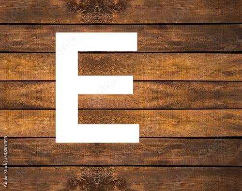 E capital letter of alphabet in white hole on wood background