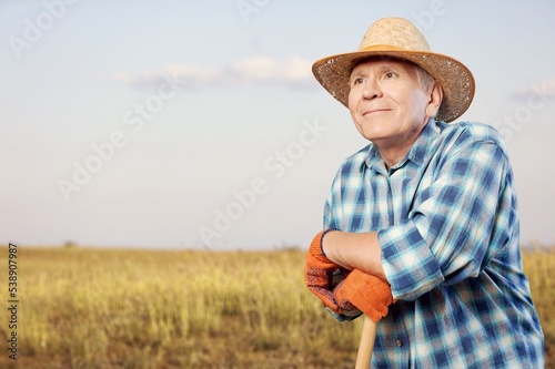 Old elderly male farmer in hat works on a field.