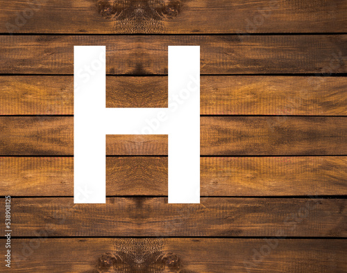 H capital letter of alphabet in white hole on wood background