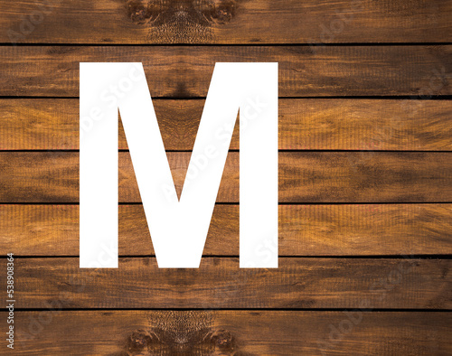 Alphabet letter M in white hole on wood background