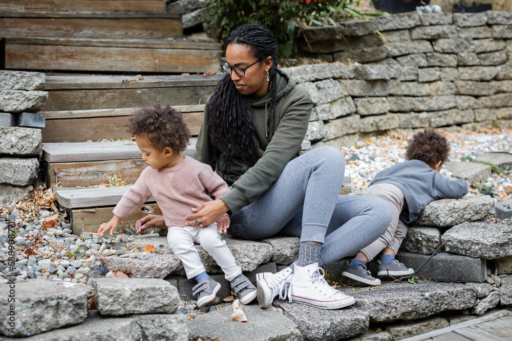 Black mom sitting with toddler twins on steps in backyard in fall 