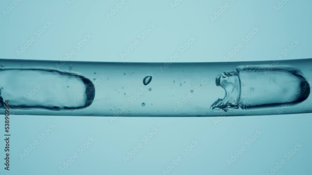 Macro shot of different sized clear bubbles flowing in glass tube with liquid on blue background. Vessel with clear liquid substance and moving bubbles. Analyzes, medicine, health.