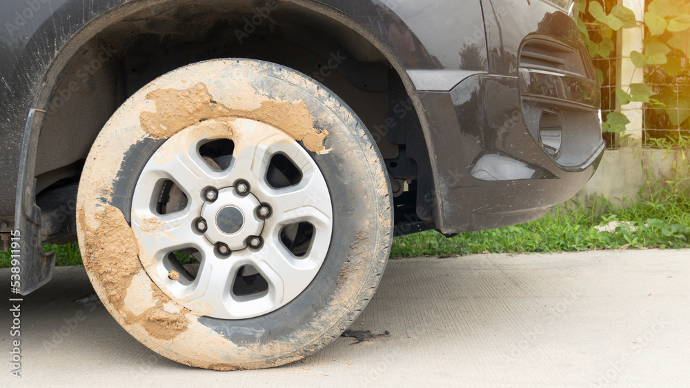 Muddy soil that clings to the surface of the tire. Front side view of cars parked on concrete road. Blurred image of a fence with green grass. Muddy soil that clings to the surface of the tire. Front side view of cars parked on concrete road. Blurred image of a fence with green grass.