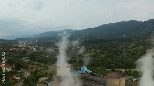 Aerial drone shot passing thru power plant chimneys, revealing mountains in the background. Paroșeni Power Station is a large electricity producer and one of the largest thermal power plants in the EU