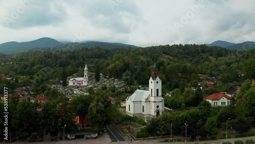 Aerial view of an old  Romanian church located in a small town between the mountains and surrounded by dense forest. Town of Lupeni, in the region of Hunedoara. White facade churches drone view. photo