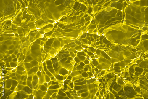 Yellow water colored clear calm water surface texture with splash, bubble. Shining yellow water ripple background. Surface of water in swimming pool. Yellow bubble water shine.