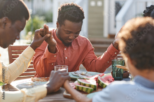 Photography Portrait of young black man saying grace at table outdoors during family gatheri