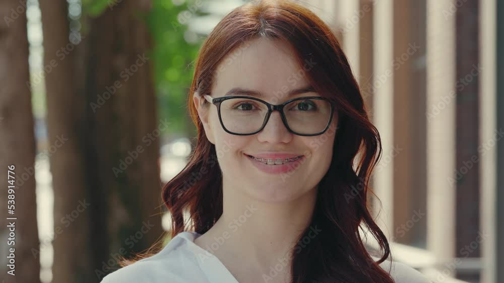 Portrait of the beautiful smiled ginger business woman wearing formal suit standing near the business centre looking at the camera in glasses. People and business concept Portrait of the beautiful smiled ginger business woman wearing formal suit standing near the business centre looking at the camera in glasses. People and business concept