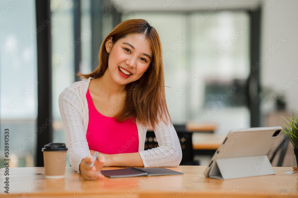 Asian female students studying online e-learning with tablet sitting at a desk and holding a pen distance learning concept at coffee shop Asian female students studying online e-learning with tablet sitting at a desk and holding a pen distance learning concept at coffee shop
