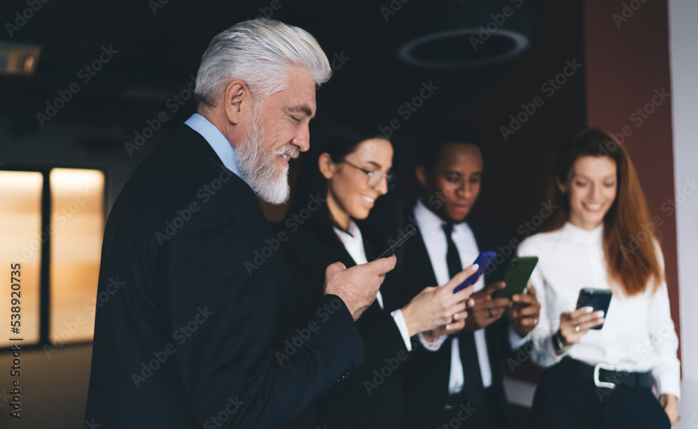 Bearded adult man browsing smartphone in modern office with group of diverse colleagues