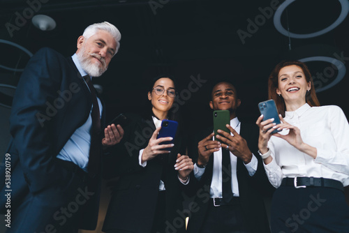 Group of diverse colleagues standing with smartphones at modern office