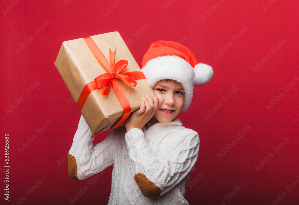 Cute little boy in a Santa Claus hat holding a gift box on a red background. a child with a New Year's gift for Christmas. new year