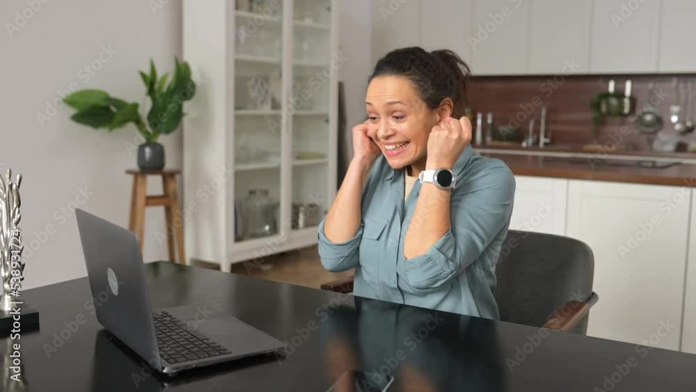 Lucky female office employee rejoicing good news or job offer. Smiling cheerful beautiful woman with curly hairstyle sitting at desk and raising fists up in sign of success Lucky female office employee rejoicing good news or job offer. Smiling cheerful beautiful woman with curly hairstyle sitting at desk and raising fists up in sign of success