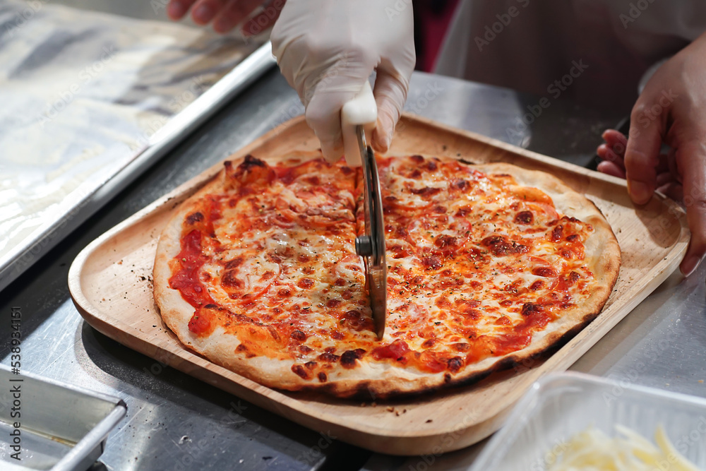 Chef cuts freshly prepared pizza slices at kitchen	