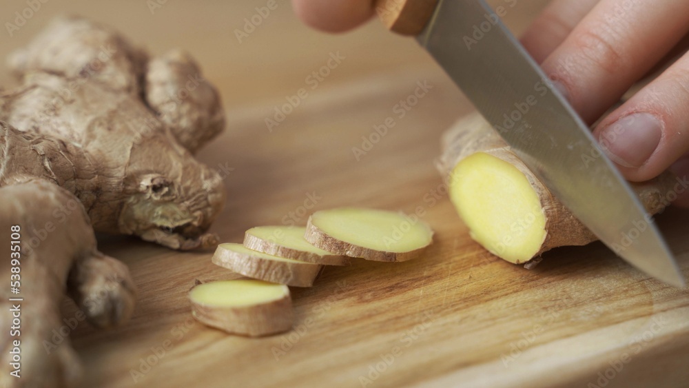 Woman cutting fresh ginger root on kitchen table Woman cutting fresh ginger root on kitchen table