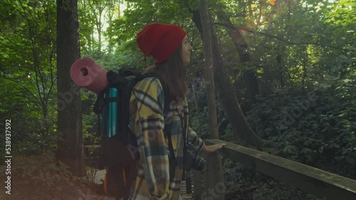 Wallpaper Mural Female adventurer in hipster shirt and red hat or travel blogger with tourist hiking backpack walks down the wooden boardwalk and looking around in green forest. Millennial traveller, travel trip Torontodigital.ca