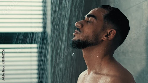 Side view Hispanic Latino Indian handsome bearded naked man guy washes in shower bath rain hot water washing male face hair refreshed after workout in gym morning hygiene procedure refreshment clean photo