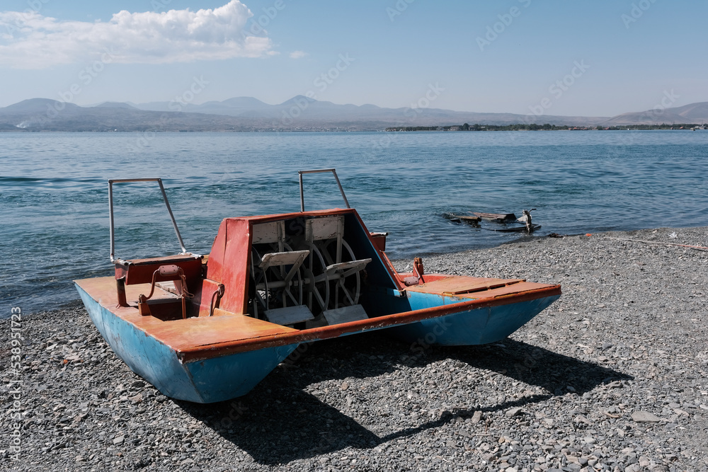 Old paddle boat (pedalo, water bike) on the pebble of Sevan lake beach on sunny summer day, Armenia.
