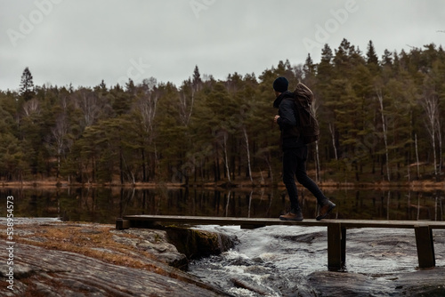 A caucasian man hiker walking on a woodenbridge over looking a lake in the forest watching reflections in the water.