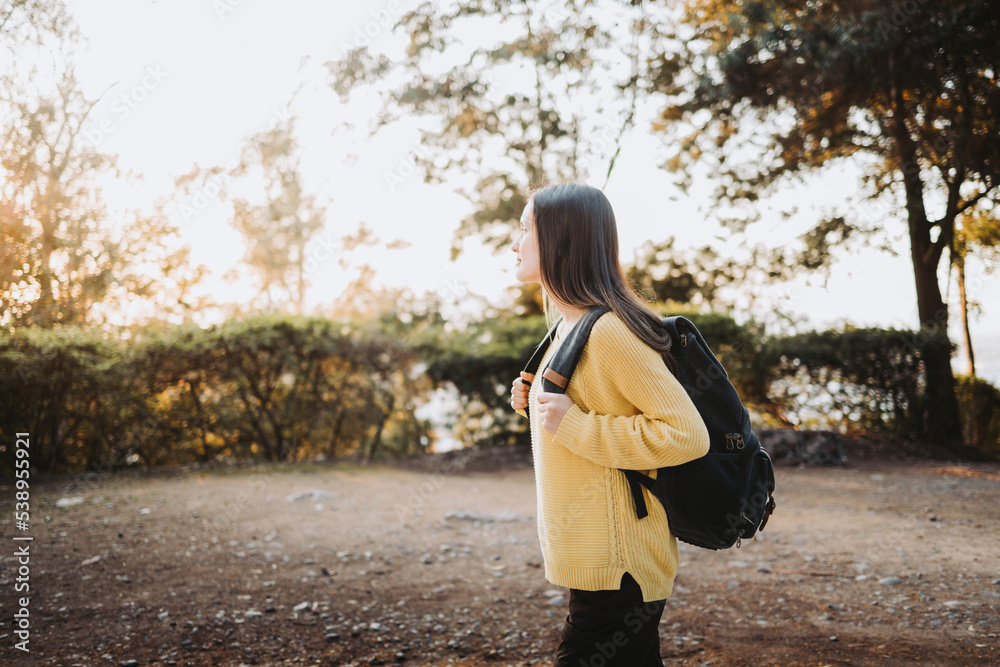 Side view female college student wearing a yellow sweater and a backpack in the campus park road. Innocent smile Side view female college student wearing a yellow sweater and a backpack in the campus park road. Innocent smile