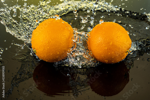 two whole oranges on dark glass with reflection