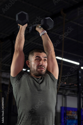 Mexican man in sportswear exercising in a gym using two dumbbells