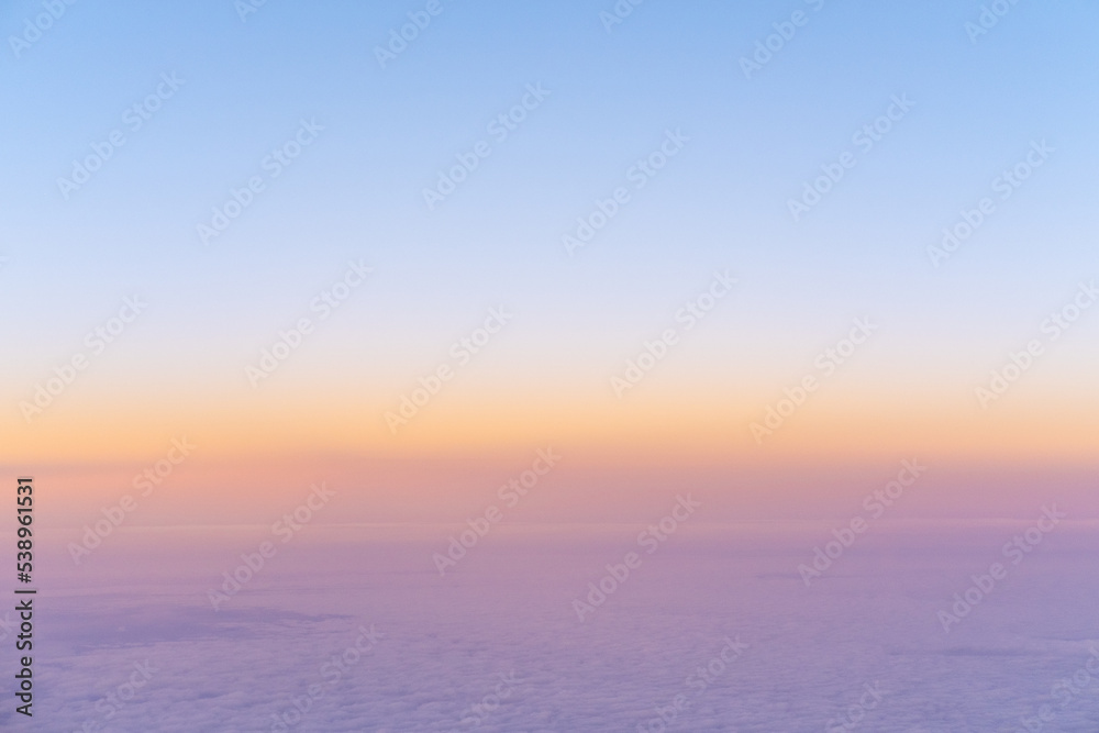 Aerial view of bright yellow sunset over pink purple dense clouds with blue sky overhead, top view from an airplane. Sky Gradient. Can be used as advertising background, overlay. Travel concept.