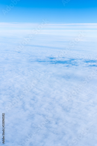 Background of a blue heavenly sky with fluffy dense clouds, top view from an airplane, vertical frame. Sky Gradient. Can be used as advertising background, overlay. Travel concept.