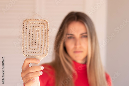 Selective focus of blond hair loss in a maze shape hair brush with unfocused young woman in the white background