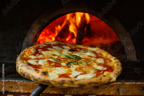 Pizza Margherita napoletana con sugo di pomodoro, mozzarella e basilico appena uscita dal forno a legna sullo sfondo photo