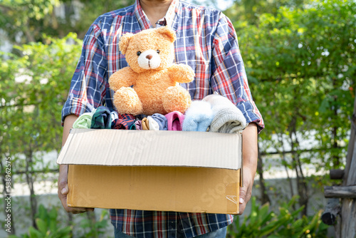 Holding clothing donation box with used clothes and doll at home to support help for poor people in the world.