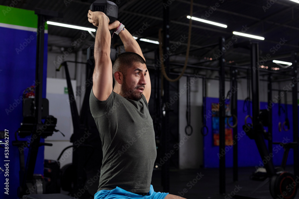 close up of a latino athlete doing triceps exercise in a gym with a dumbbell close up of a latino athlete doing triceps exercise in a gym with a dumbbell