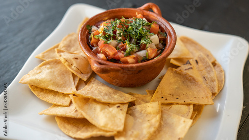 delicious Mexican dish "pico de gallo". With natural vegetables, onion, tomatoes, and parsley. served with nachos. Black background. Vegan food © Viktoriia