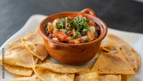 delicious Mexican dish "pico de gallo". With natural vegetables, onion, tomatoes, and parsley. served with nachos. Black background. Vegan food