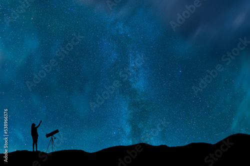 Girl silhouette stands on the hill with telescope on and looks on the milky way galaxy. Dark starry night.